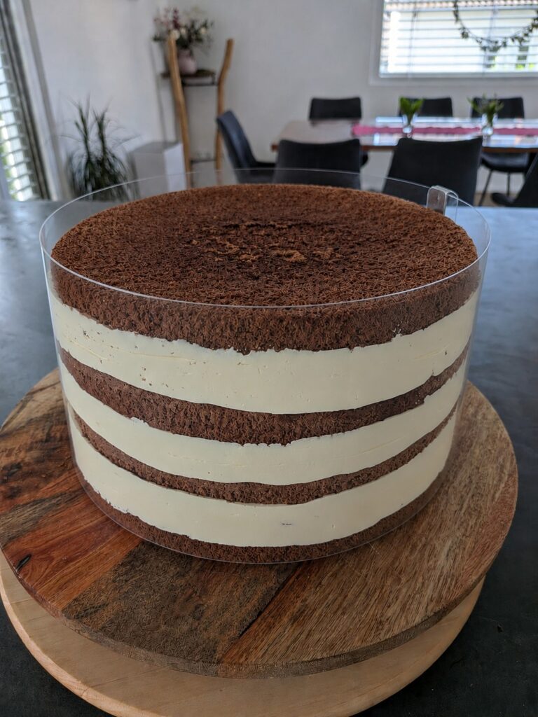 Geschichtete Schoko-Biskuit-Torte mit Cremefüllung in einer eng anliegenden Tortenrandfolie.